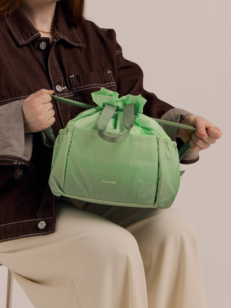 Model cinching CALPAK Insulated Lunch Bag in ombre green Matcha to close