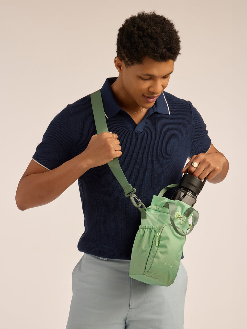 Model wearing green shoulder strap of CALPAK Water Bottle Holder in green ombre Matcha