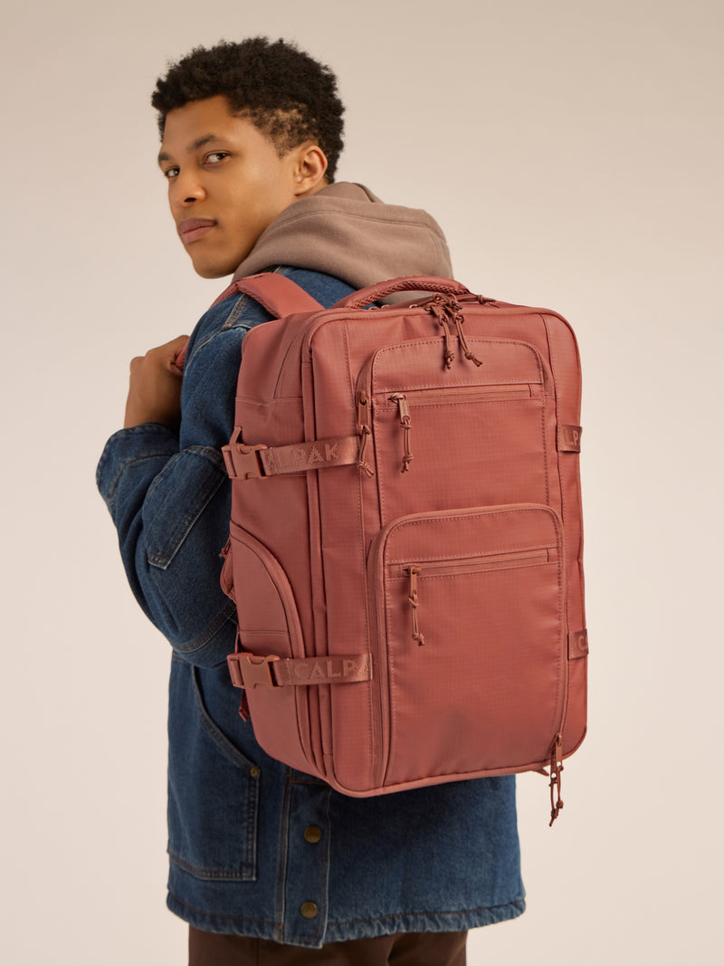 Model wearing the CALPAK Terra 26L Laptop Backpack Duffel in red and orange Matte Clay