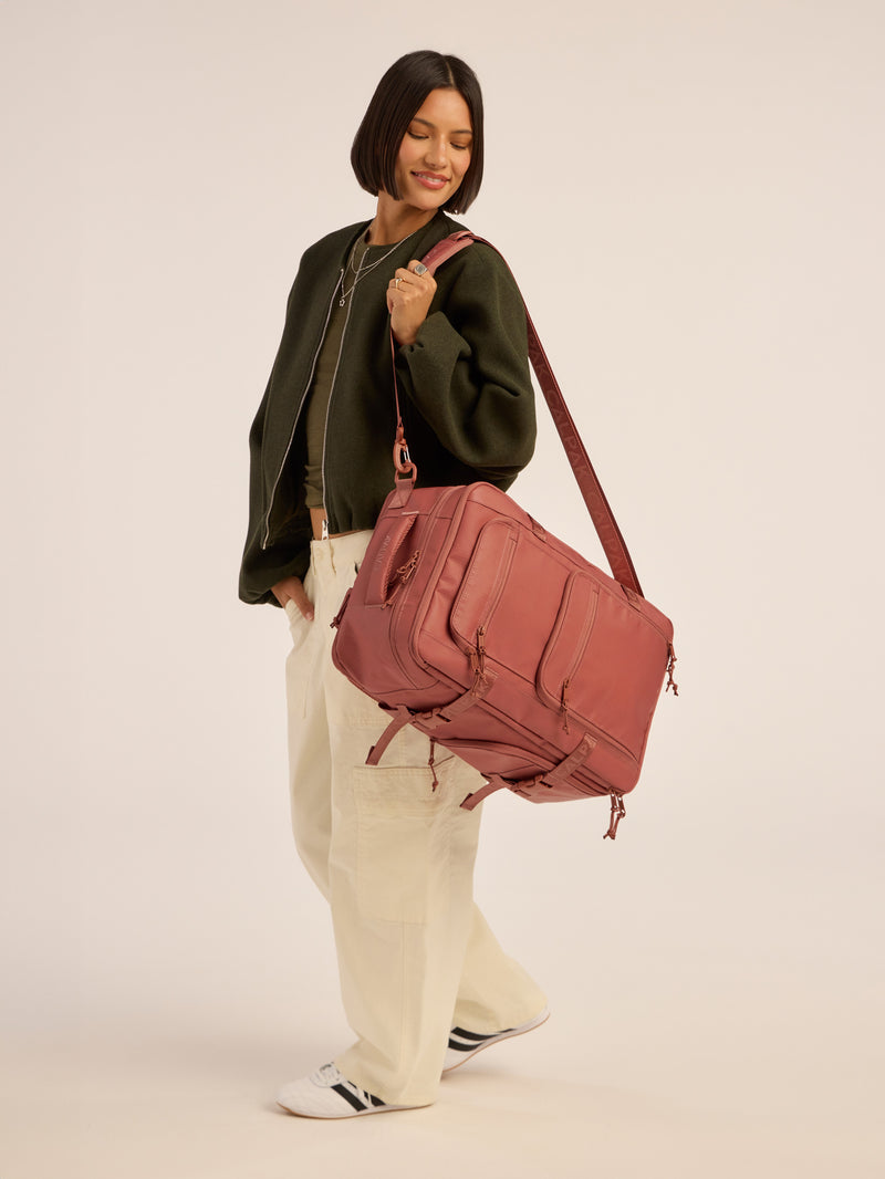 Model wearing CALPAK Terra 26L Laptop Backpack Duffel in red and orange Matte Clay duffel