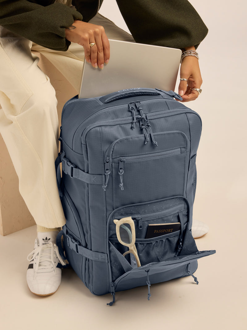 Model putting in laptop into the CALPAK Terra 26L Laptop Backpack Duffel in blue Matte Indigo