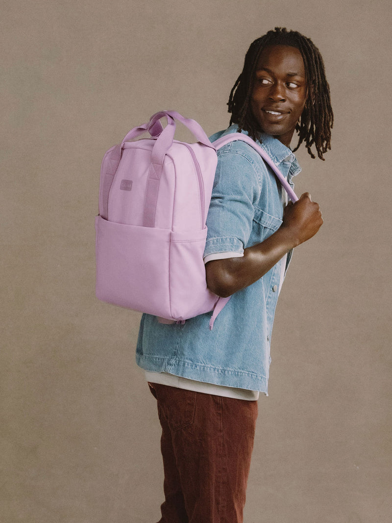 Model wears CALPAK Connect Laptop Backpack in berry on back