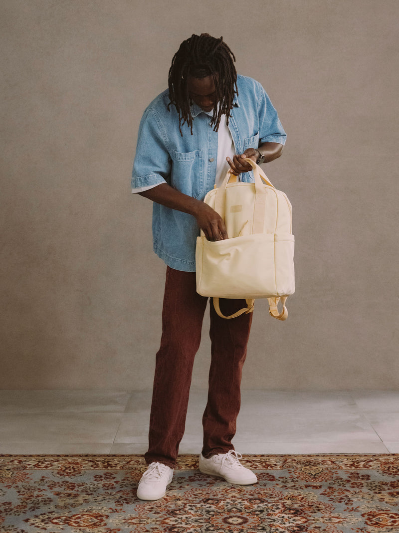 Model searches for belongings within front pocket of sunshine yellow CALPAK Connect Laptop Backpack