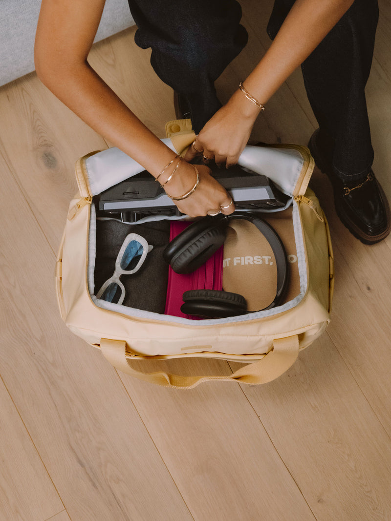 Model placing DJ set within padded laptop sleeve of CALPAK Connect Laptop Duffel with other belongings within in sunshine yellow