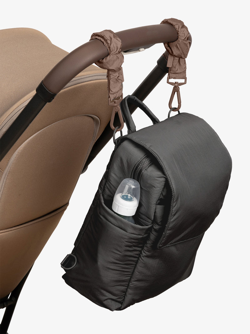 CALPAK Convertible Mini Diaper Backpack in Black with Brown Hazelnut Stroller Straps attached to a brown stroller