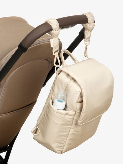 CALPAK Convertible Mini Diaper Backpack attached to stroller by CALPAK Stroller Straps in beige oatmeal