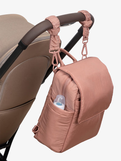 CALPAK Convertible Mini Diaper Backpack attached to stroller by CALPAK Stroller Straps in pink peony; BPC2401-PEONY, BBPC2401-PEONY
