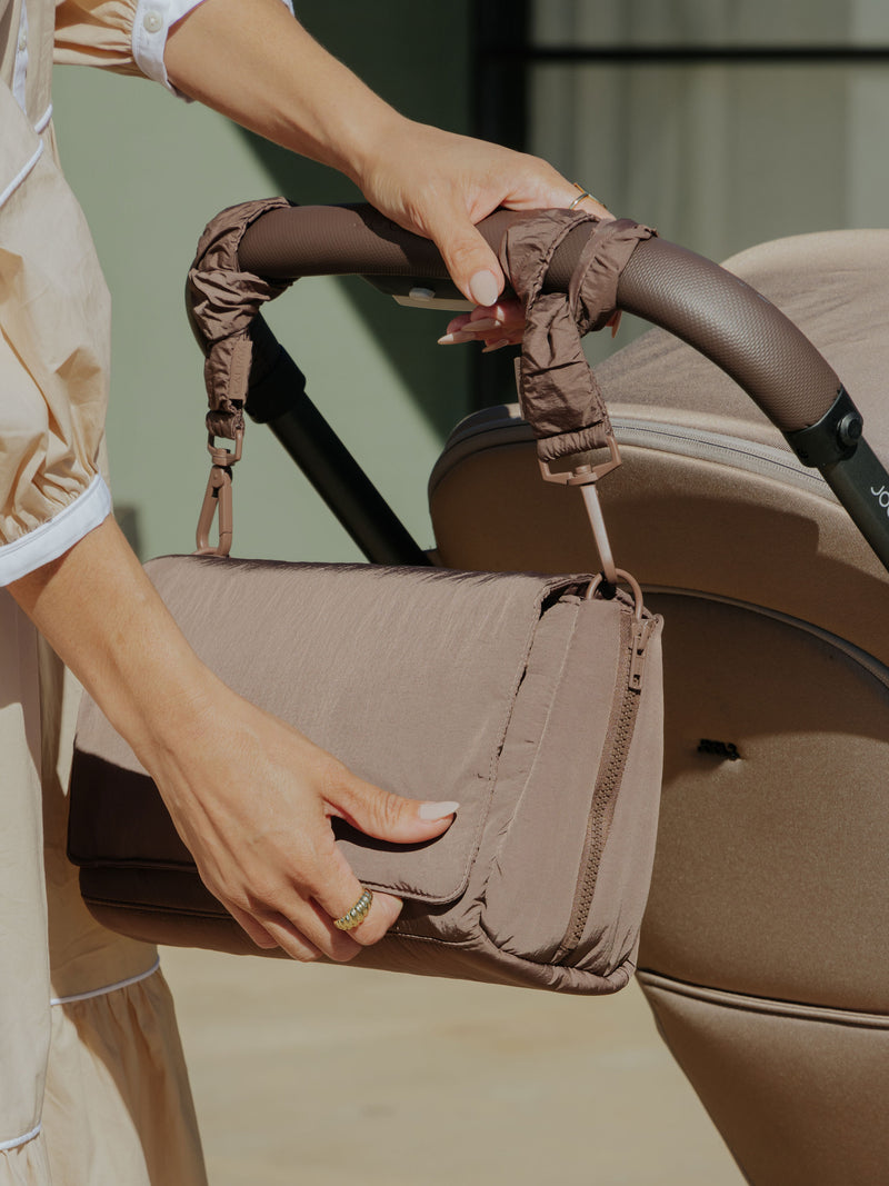 Model displaying CALPAK Convertible Stroller Caddy Crossbody attached to stroller by Stroller Straps in brown