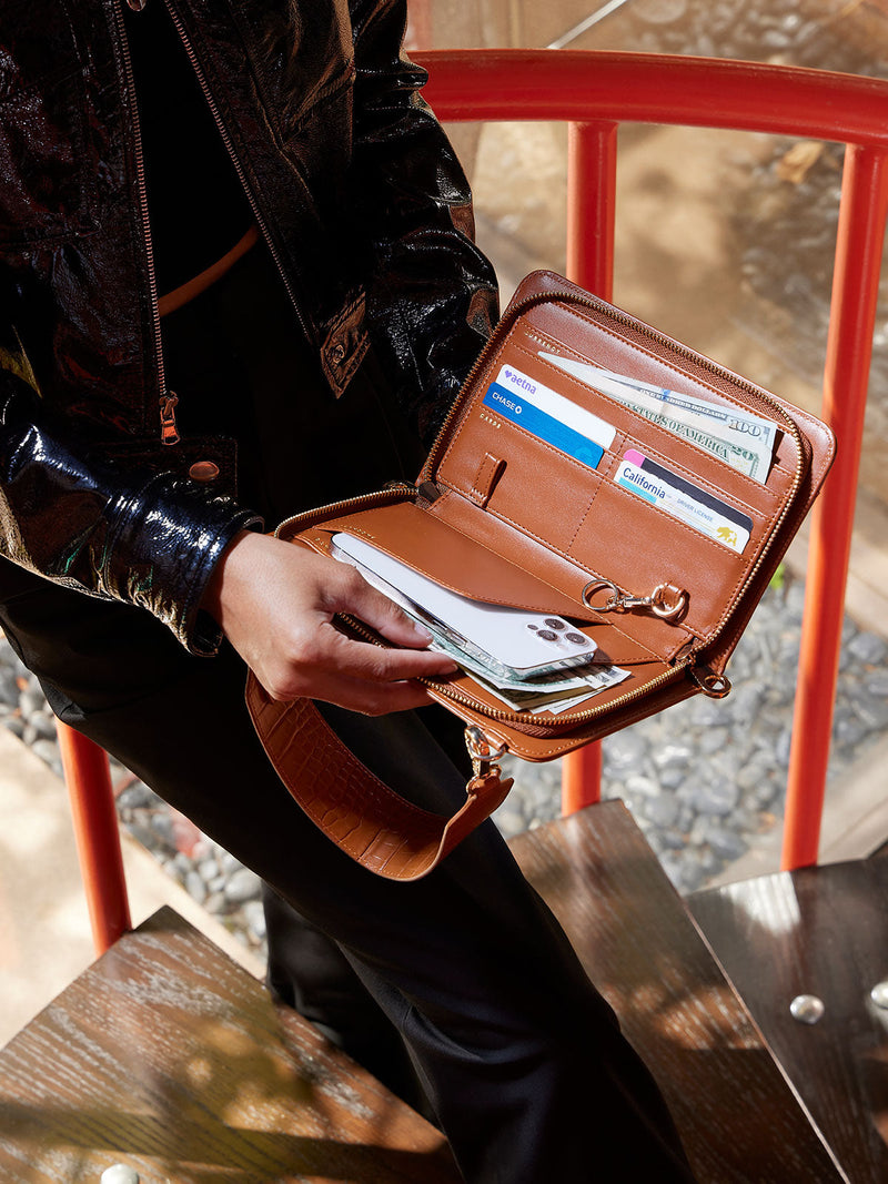 Model displaying interior of CALPAK Croc Wallet featuring multiple pockets for cards, travel documents, and cellphone in brown cognac; TWC2201-COGNAC-EA