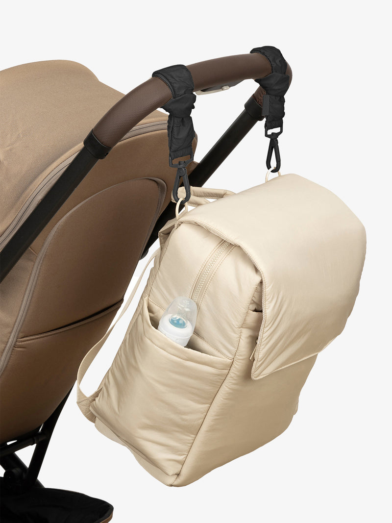 CALPAK Diaper Backpack in white Oatmeal with Black Stroller Straps attached to a brown stroller