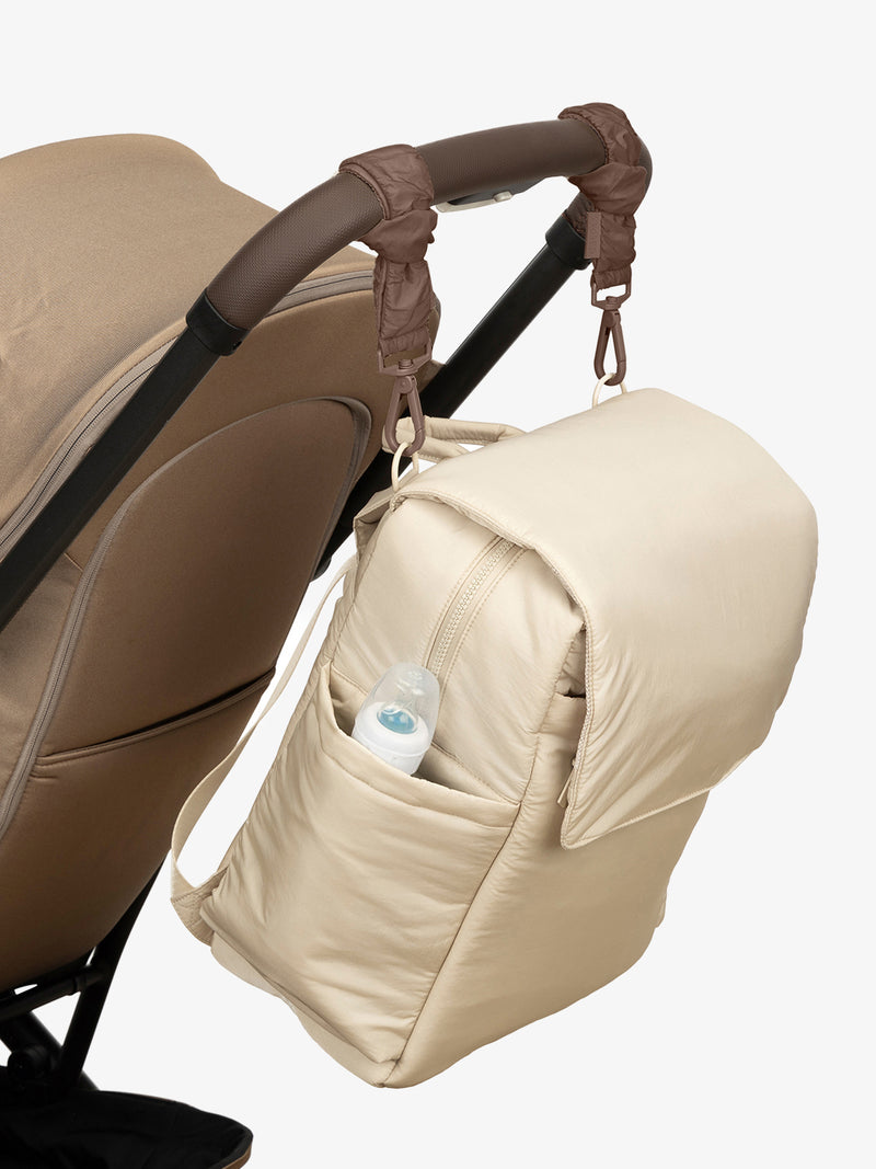 CALPAK Diaper Backpack in white Oatmeal with brown Hazelnut Stroller Straps attached to a brown stroller