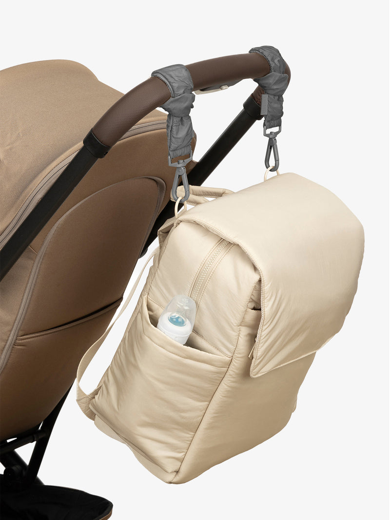 CALPAK Diaper Backpack in white Oatmeal with grey Slate Stroller Straps attached to a brown stroller