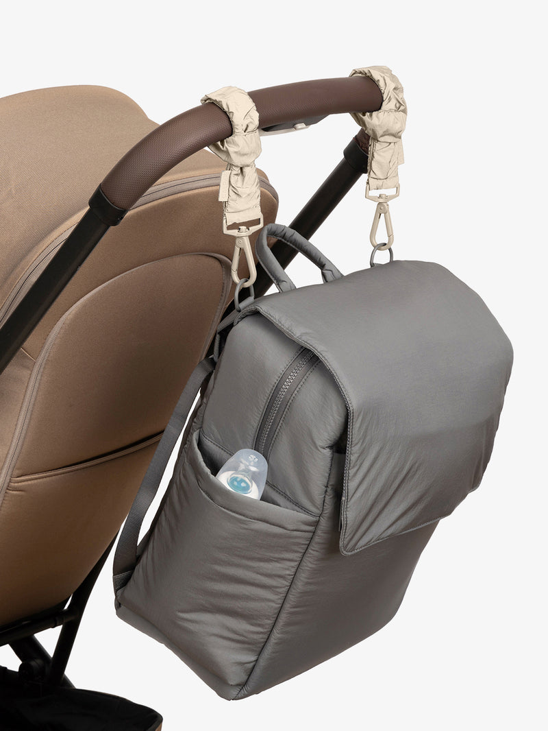 CALPAK Diaper Backpack in grey Slate with white Oatmeal Stroller Straps attached to a brown stroller