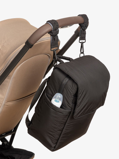 CALPAK Diaper Backpack with Laptop Sleeve attached to stroller by CALPAK Stroller Straps in black; BPB2401-BLACK, BBPB2401-BLACK