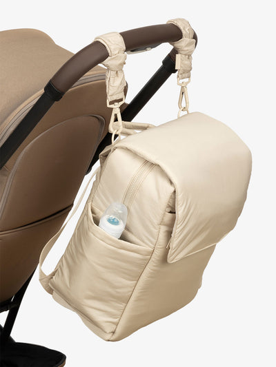 CALPAK Diaper Backpack with Laptop Sleeve attached to stroller by CALPAK Stroller Straps in oatmeal; BPB2401-OATMEAL, BBPB2401-OATMEAL