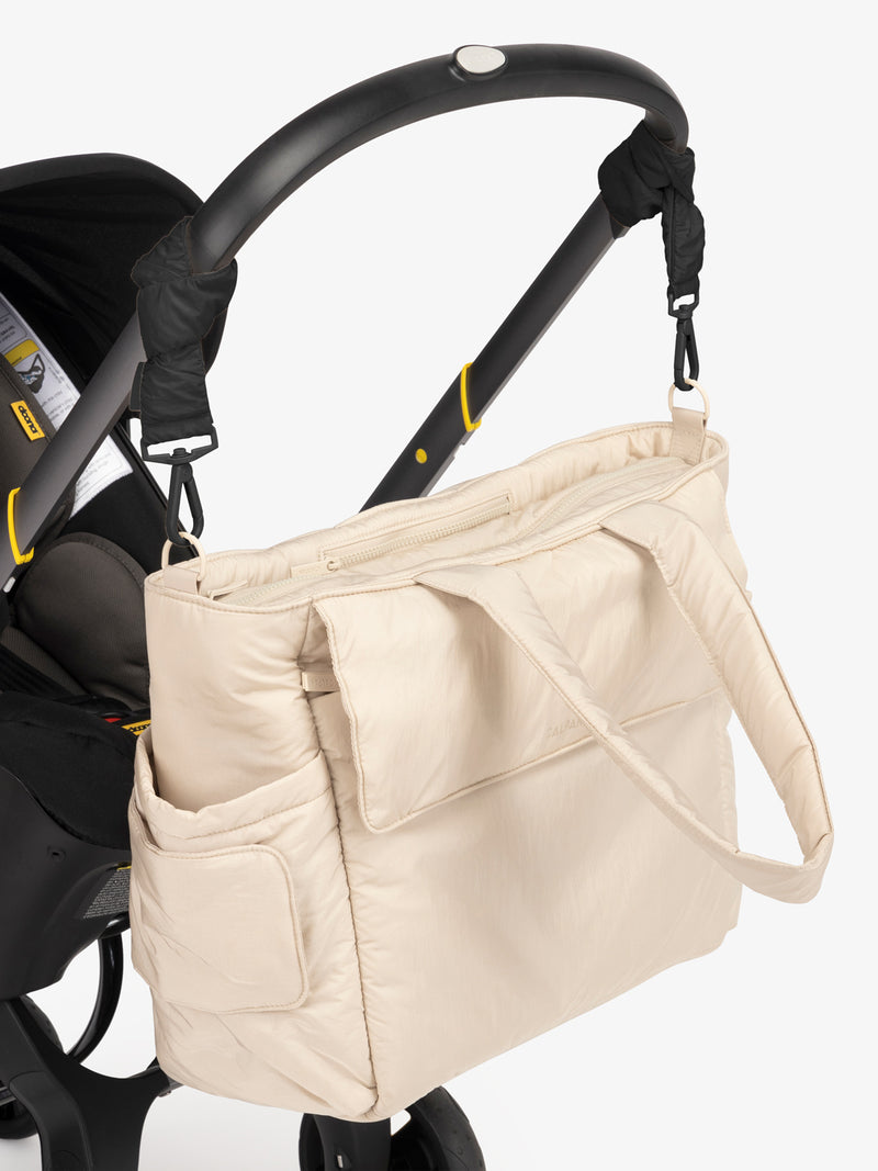 CALPAK Diaper Tote Bag in white Oatmeal with Black Stroller Straps attached to a black stroller