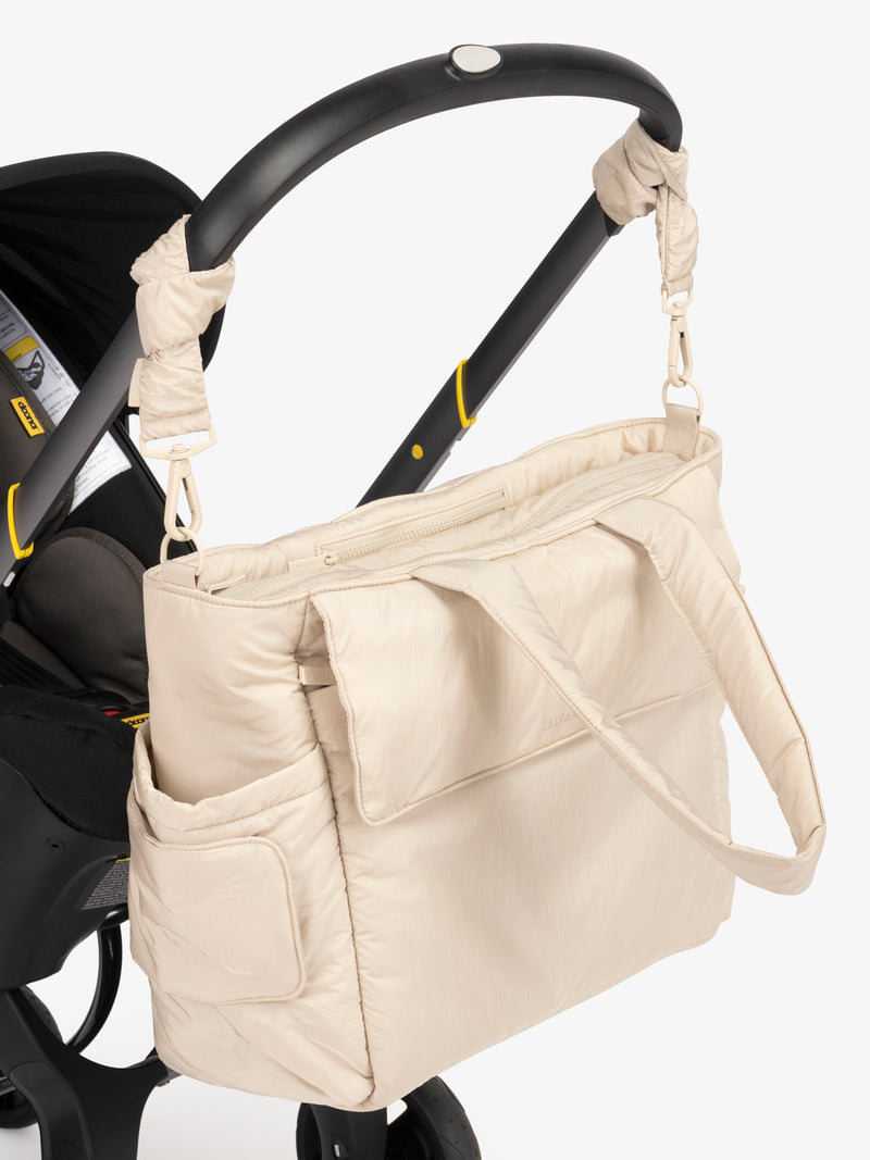 CALPAK Diaper Tote Bag in white Oatmeal with white Oatmeal Stroller Straps attached to a black stroller