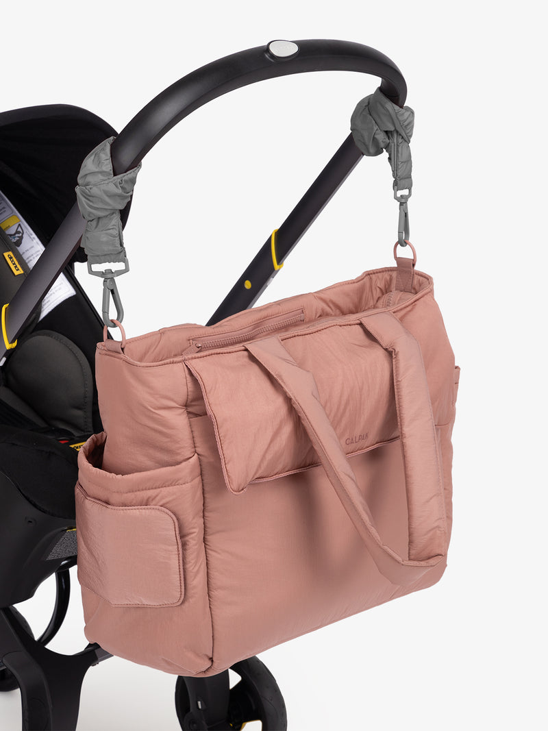 CALPAK Diaper Tote Bag in pink Peony with grey Slate Stroller Straps attached to a black stroller