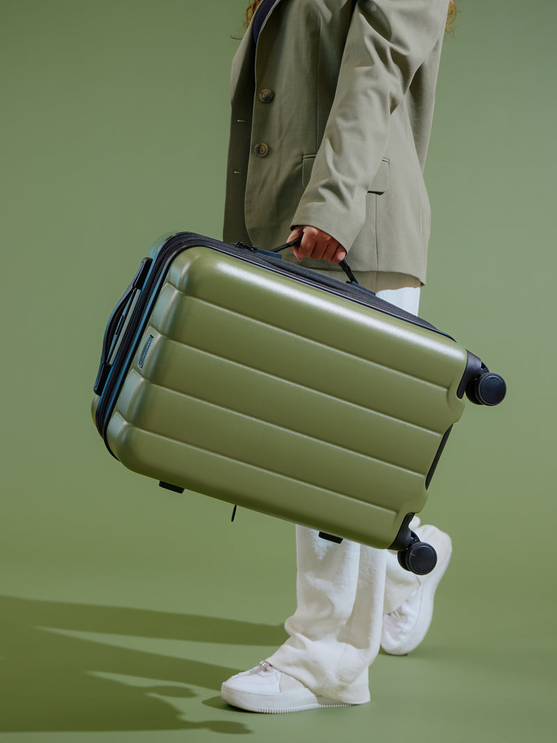 Model holding green pistachio CALPAK Evry Carry-On Luggage by side handle