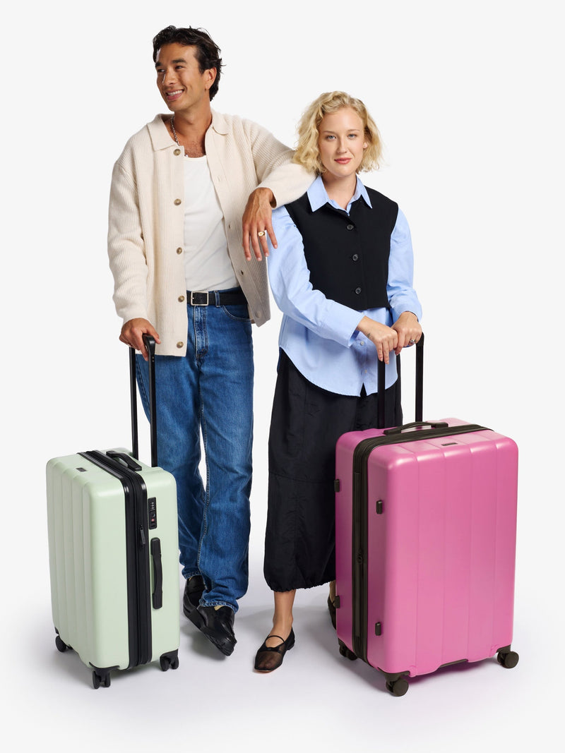 Models standing besides CALPAK Evry Medium Luggage in raspberry and Evry Carry-On Luggage in light green daisy