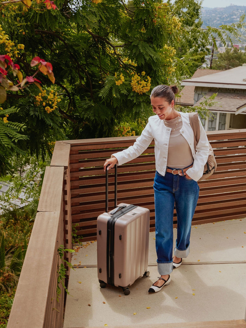 Model standing besides CALPAK Evry Medium Luggage in chocolate