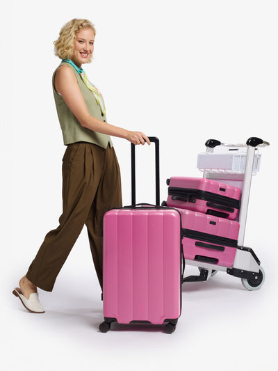 Modeling rolling CALPAK Evry Medium Luggage in pinkish red raspberry