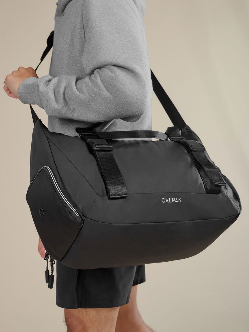 Model displaying CALPAK Fit Gym Bag with padded, adjustable shoulder strap and adjustable yoga mat straps in black