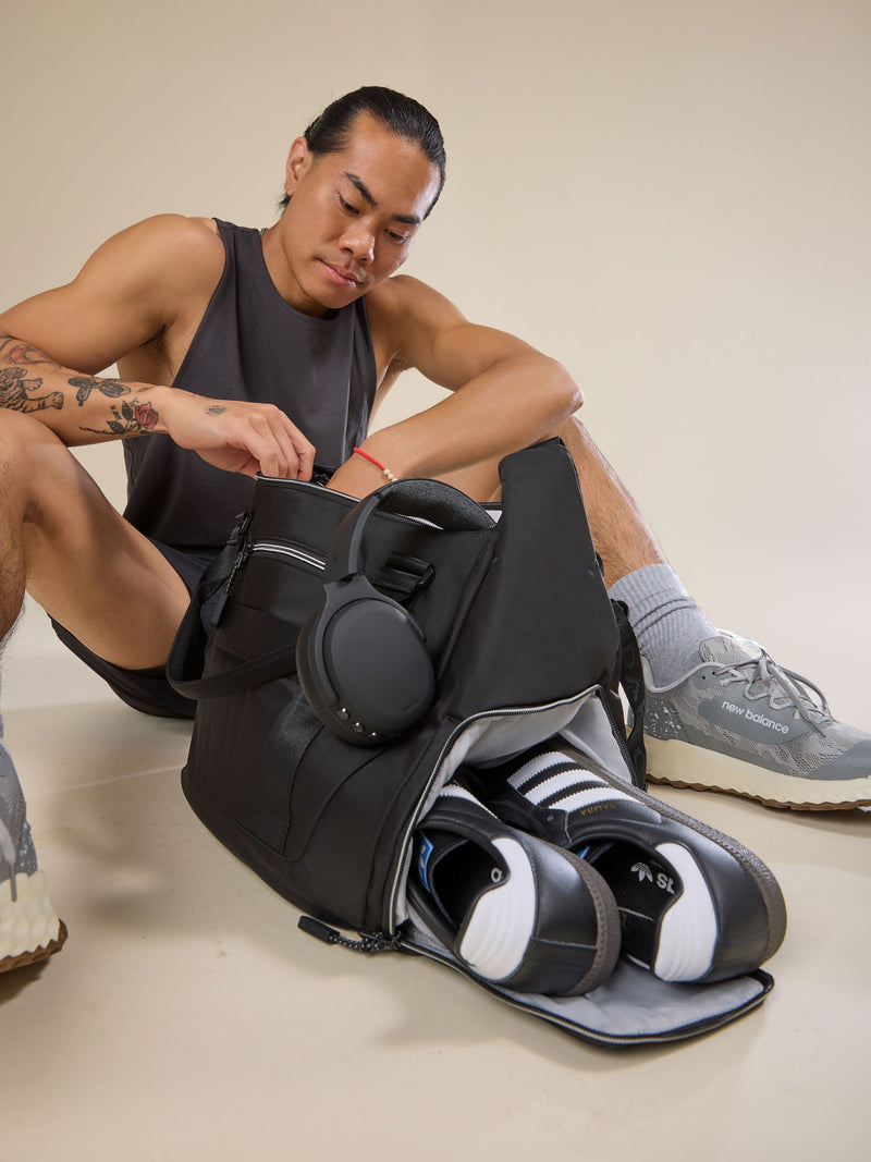 Model displaying separate shoe compartment of black CALPAK Fit Gym Bag