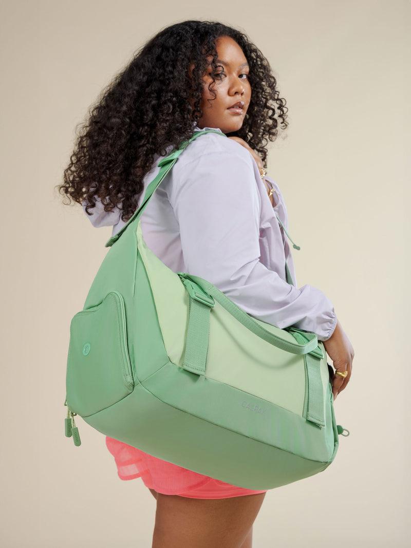 Model wearing adjustable shoulder strap of CALPAK Fit Gym Bag in sage green