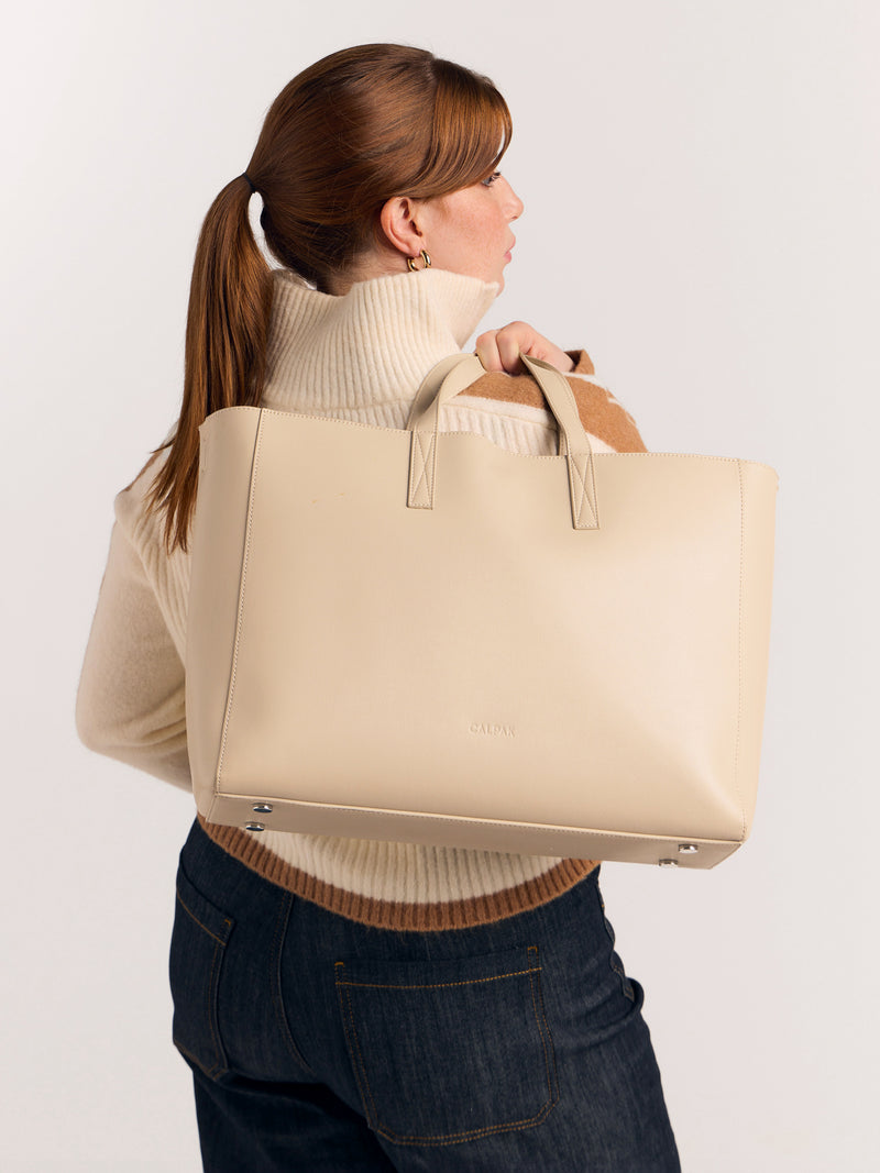 CALPAK Haven Laptop Tote Bag in light beige Birch with zoomed in image of model carrying it over the shoulder with shoulder strap