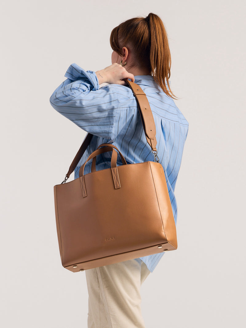 CALPAK Haven Laptop Tote Bag in brown Toffee with zoomed in image of model carrying it on shoulder with shoulder strap