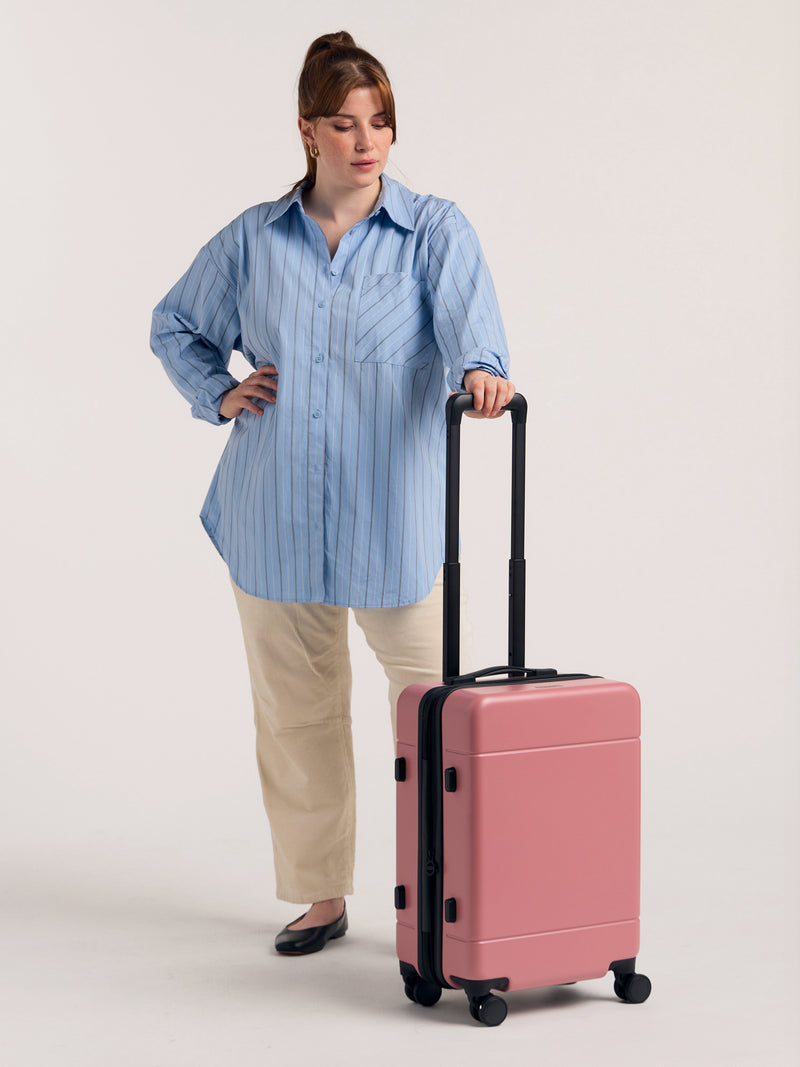 Model with CALPAK Hue hard shell rolling carry on luggage in light pink mauve