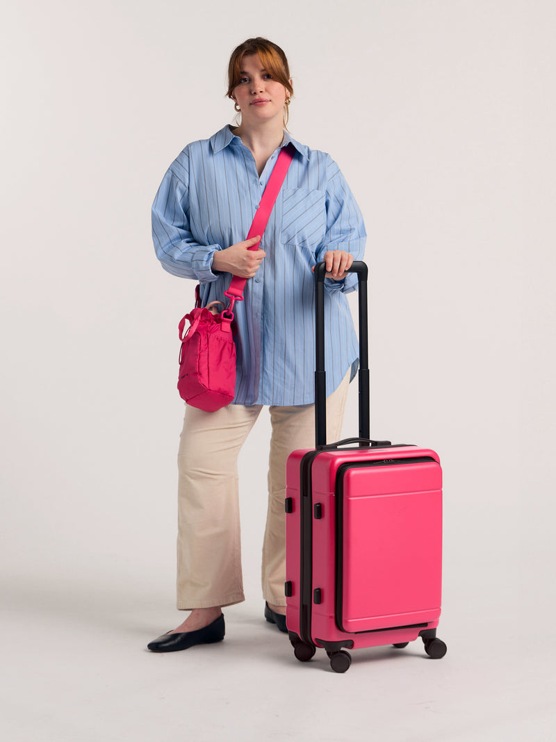 Model with CALPAK Hue Front Pocket Carry-On Luggage with hard shell carry-on spinner luggage with front-laptop compartment in Dragonfruit