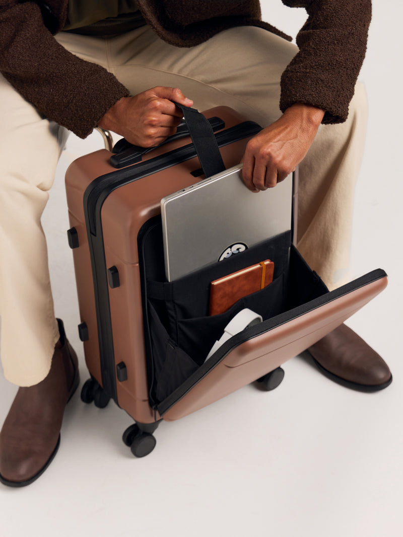 Front-laptop compartment with model putting in laptop in the CALPAK Hue Front Pocket Carry-On Luggage in Hazel