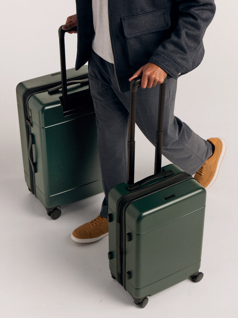 Model rolling the CALPAK Hue Medium and Large Luggage in green Emerald