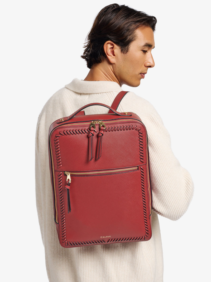 Model wearing CALPAK 15 inch laptop backpack with exterior zippered pocket in red