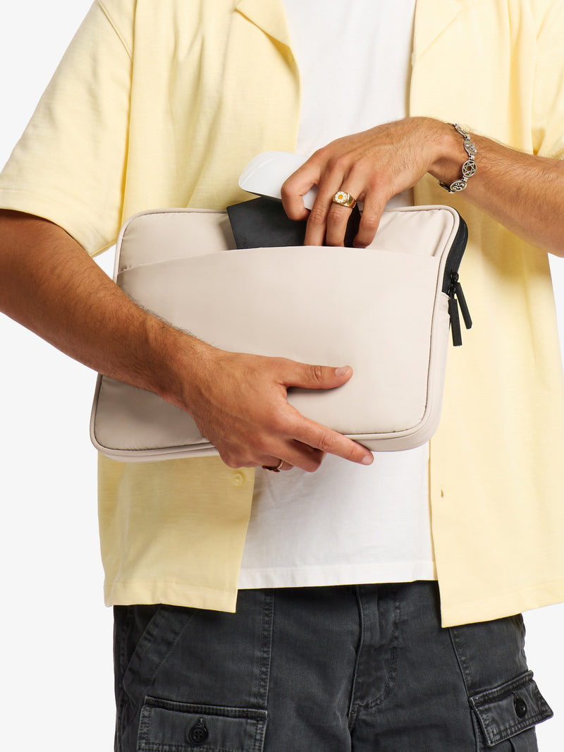 Model placing mouse and wallet into back pocket of CALPAK Luka 14" Padded Laptop Sleeve in oatmeal