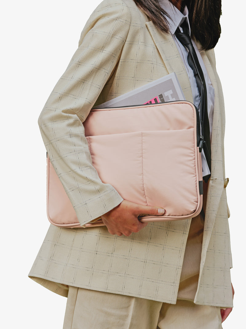 Model holding CALPAK Luka 14" Padded Laptop Sleeve with magazine under right arm in pink rose quartz