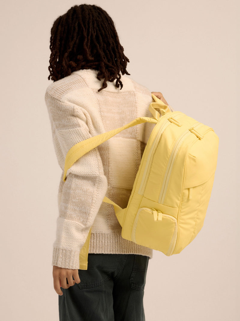 Model placing adjustable shoulder straps of yellow CALPAK Luka 15 inch Laptop Backpack over shoulders