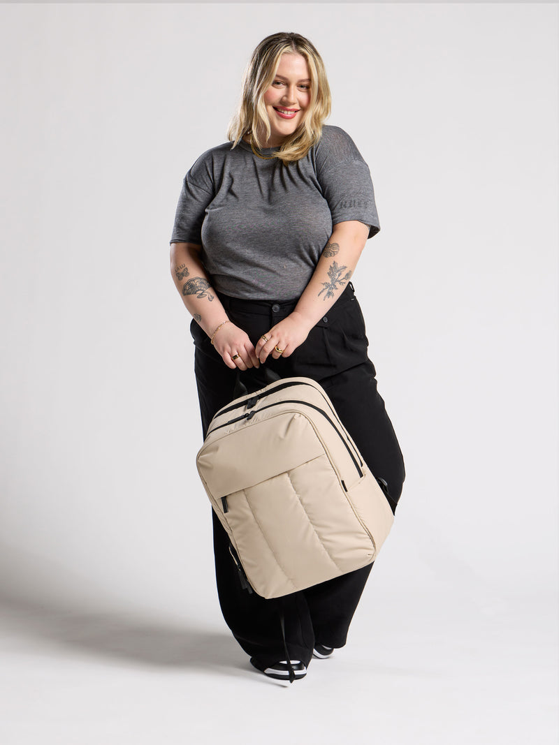 Model holding CALPAK 17 inch Laptop Backpack in beige oatmeal