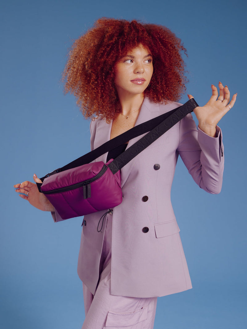 Model holding CALPAK Luka Belt Bag in plum by adjustable strap