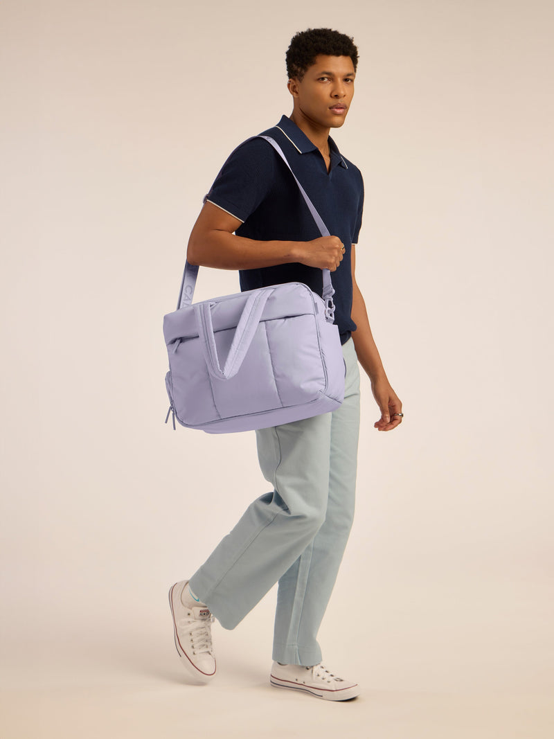 Male model holding CALPAK Luka Duffel monochrome in purple lavender Orchid by shoulder strap