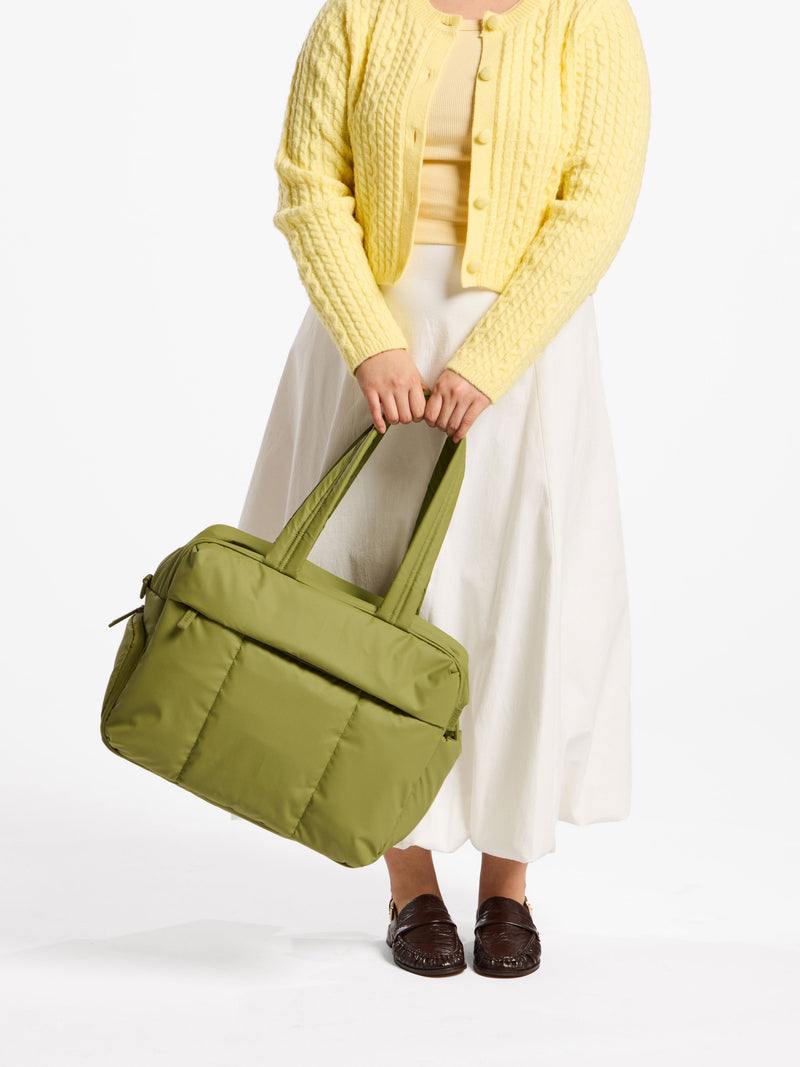 Model holding CALPAK luka duffel by straps in green