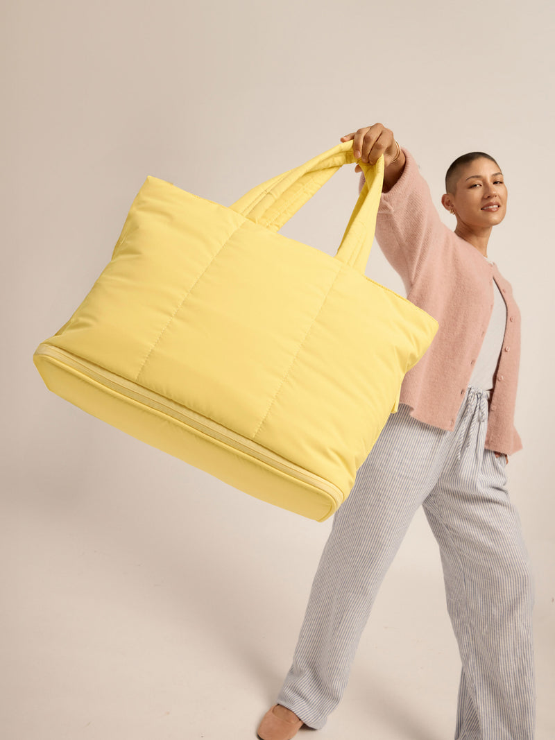 Model holding CALPAK Luka Expandable Laptop Tote by carrying handle in butter yellow