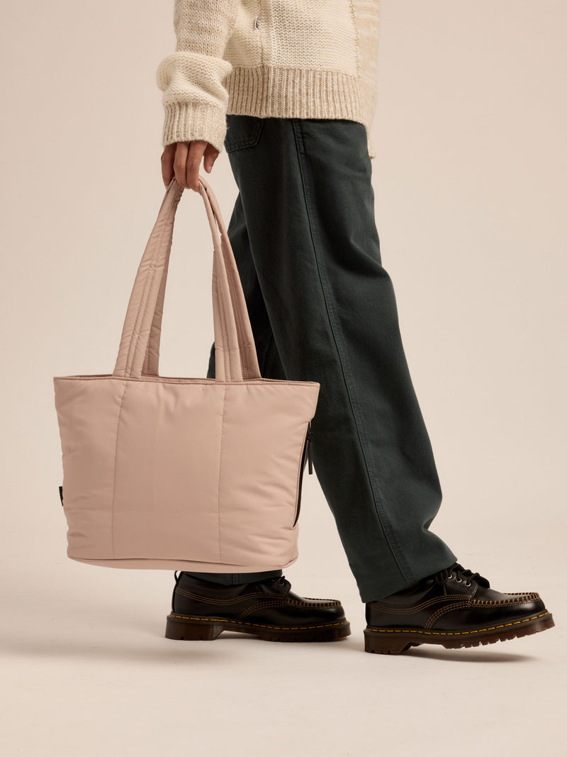 Model walking and holding CALPAK Luka Mini Tote by durable, padded shoulder strap in rose quartz pink