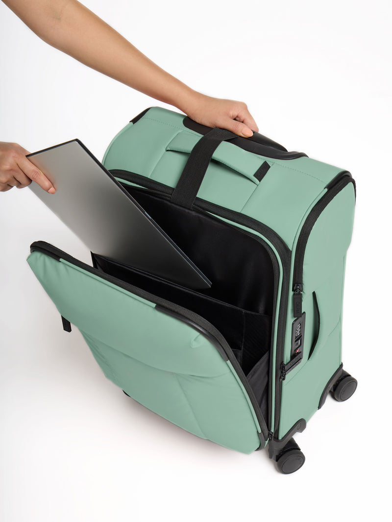 Model placing laptop in front pocket of CALPAK Luka Soft-Sided Carry-On Luggage in green