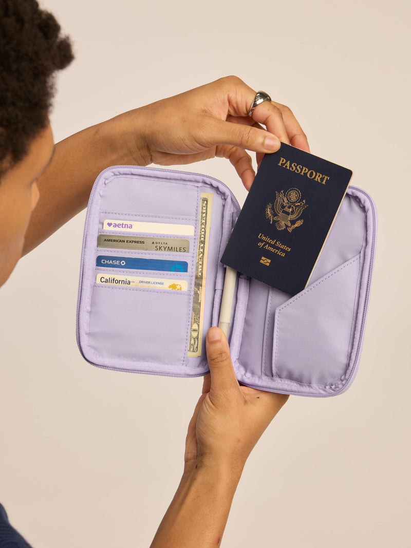 Model holding opened CALPAK Luka Passport Zippered Wallet with cards and passport in lavender purple Orchid