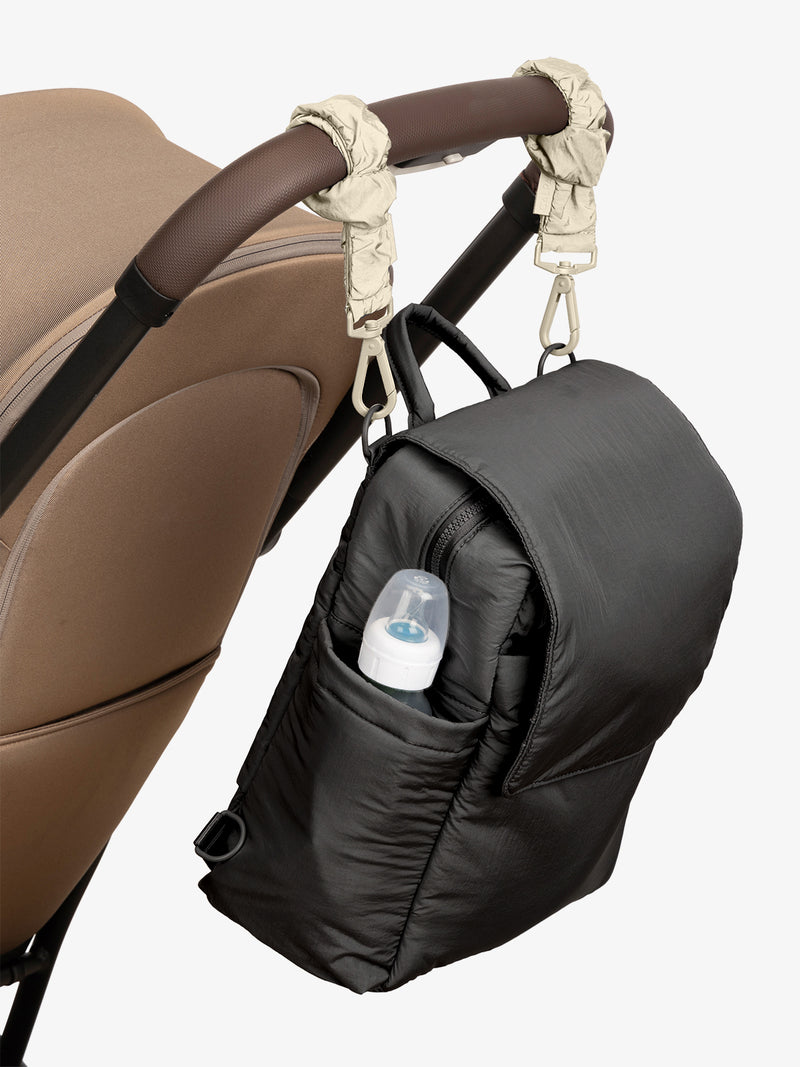 CALPAK Convertible Mini Diaper Backpack in Black with White Oatmeal Stroller Straps attached to a brown stroller