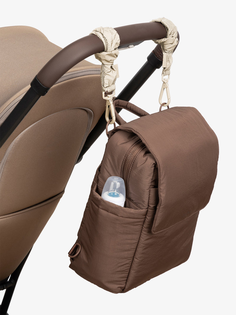 CALPAK Convertible Mini Diaper Backpack in brown Hazelnut with white Oatmeal Stroller Straps attached to a brown stroller