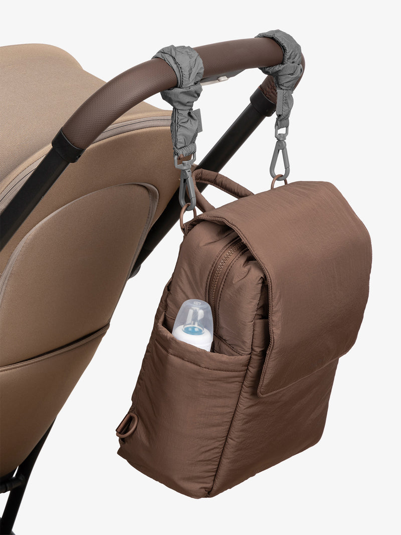 CALPAK Convertible Mini Diaper Backpack in brown Hazelnut with grey Slate Stroller Straps attached to a brown stroller